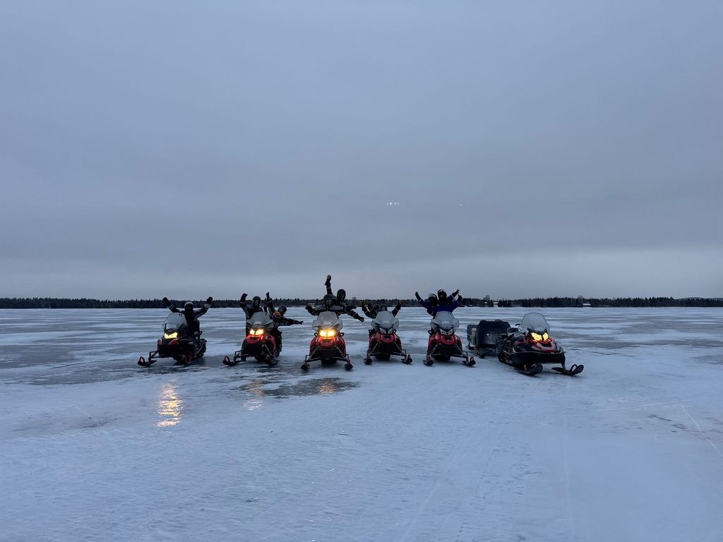 Un grupo de viajeros levanta los brazos sobre sus motos de nieve en un lago helado de Laponia