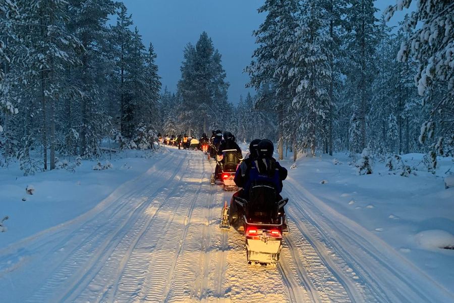 Fila de motos de nieve con los faros encendidos en un bosque al anochecer